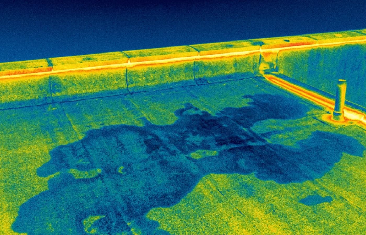 Radiometric thermal image of a flat roof and parapet, with a cool irregular patch of trapped moisture under the covering and a warm line at a service penetration